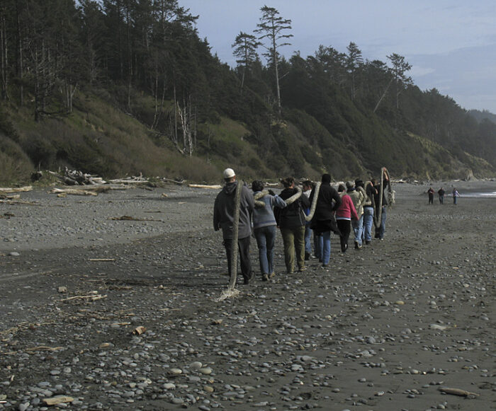 People work together to carry a heavy rope off the beach.